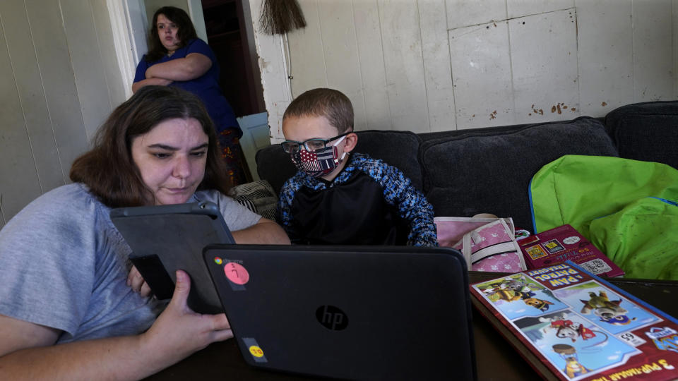 Christi Brouder, left, assists her son Wyatt, a kindergarten student with special needs, while her children distance learn due to the COVID-19 outbreak, in a makeshift classroom in the living room at the family home, Wednesday, Oct. 14, 2020, in Haverhill, Mass. Brouder has four children that are remote learning. Many families with multiple students, some with special needs, are dealing with the challenges of remote distance learning in their home. (AP Photo/Charles Krupa)