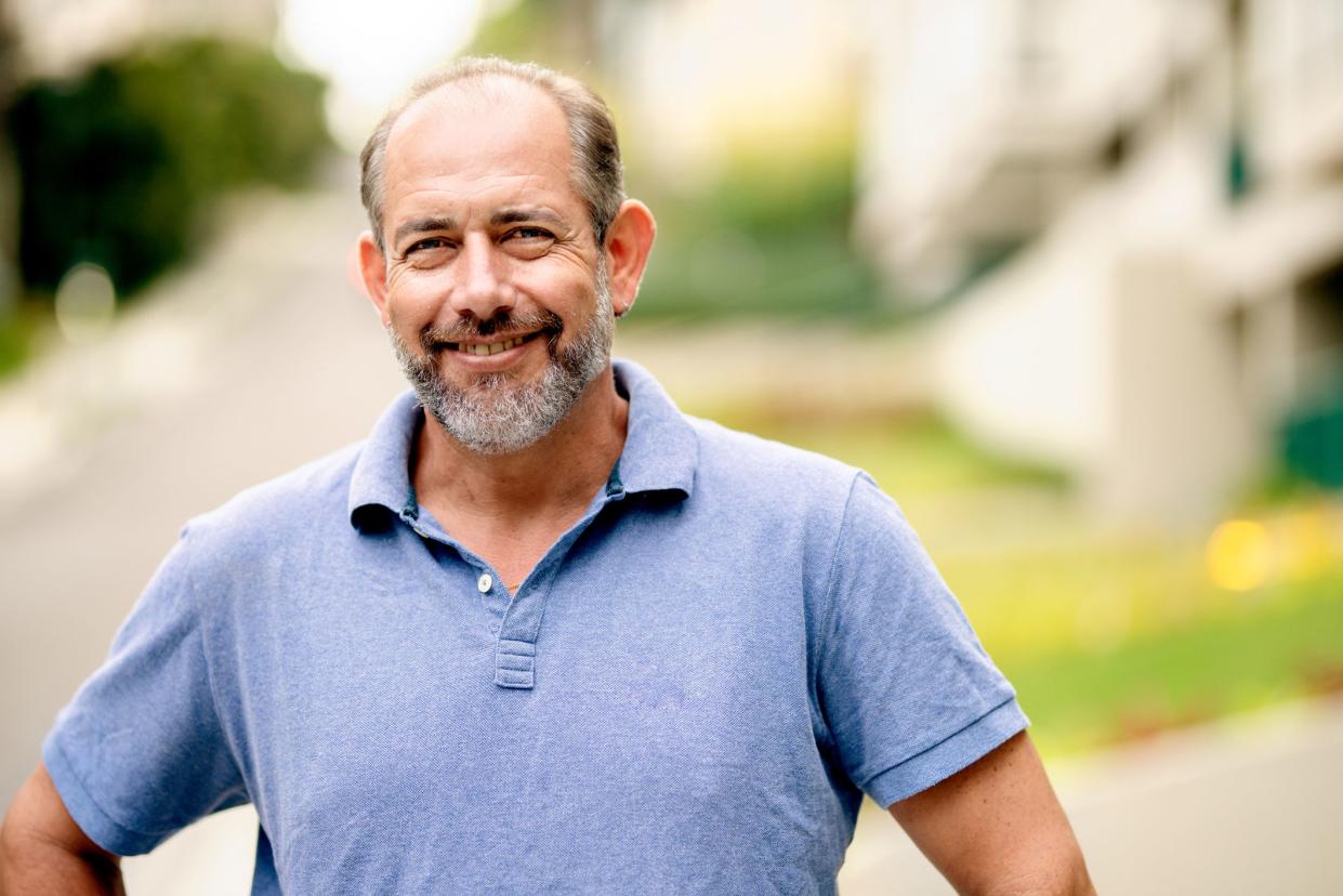 Portrait of a mature man smiling confidently while standing with his hands on his hips outside on a sidewalk in summer