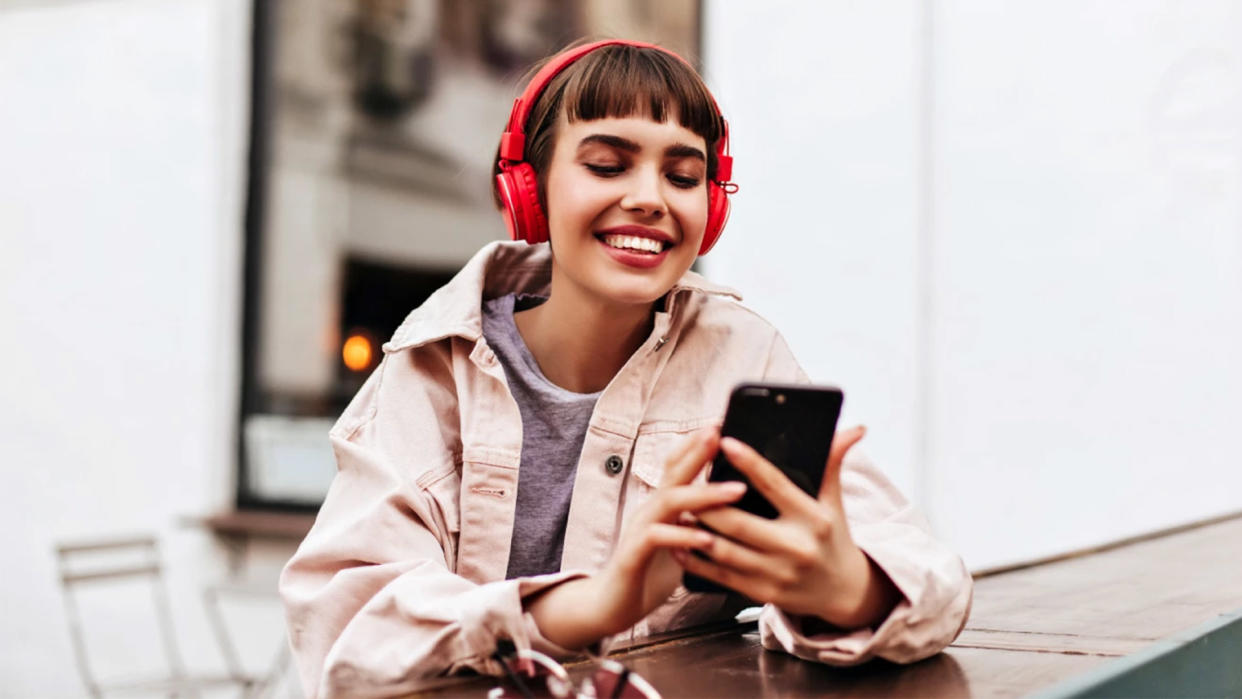  A girl looks at her phone while wearing headphones. 