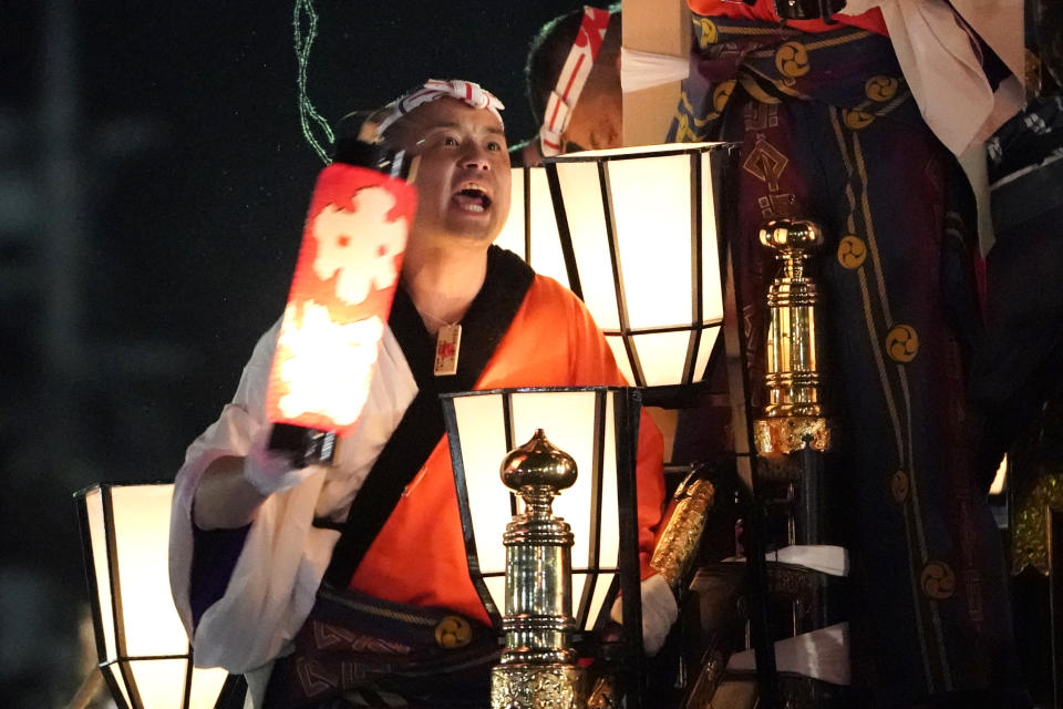 In this Tuesday, Dec. 3, 2019, photo, a man holding a lantern shouts on a lantern-covered float going to the town central square during the Chichibu Night Festival in Chichibu, north of Tokyo, Japan. Moving six towering floats up a hill and into the town center is the culminating moment of a Shinto festival that has evolved from a harvest thanksgiving into a once-a-year meeting between two local gods. (AP Photo/Toru Hanai)