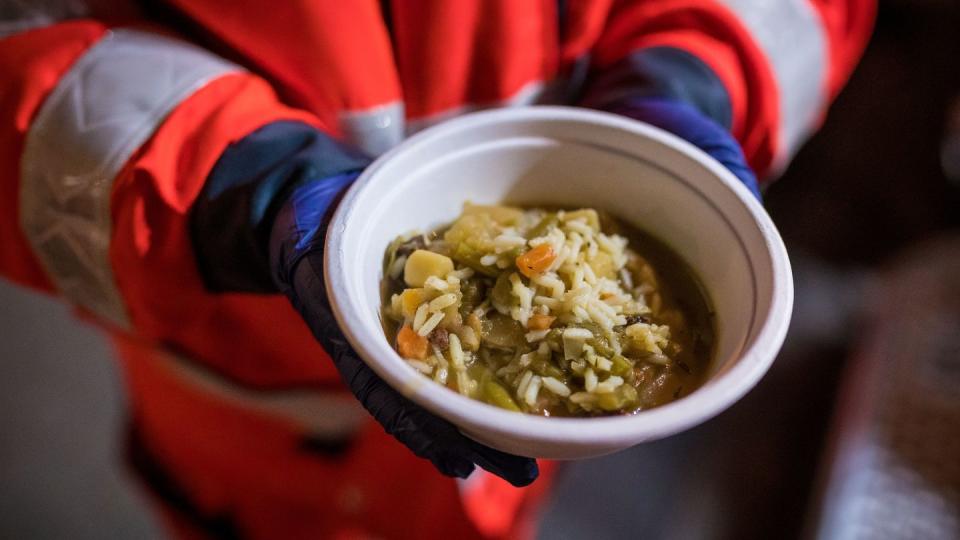 Mensch in Rettungssanitäter-Uniform (Körper ab Brust abwärts) hält Schüssel mit Essen in den Händen