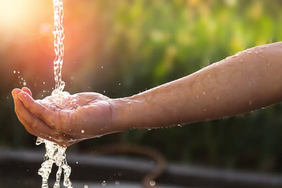 Someone putting their hand under a stream of water from an outside faucet.