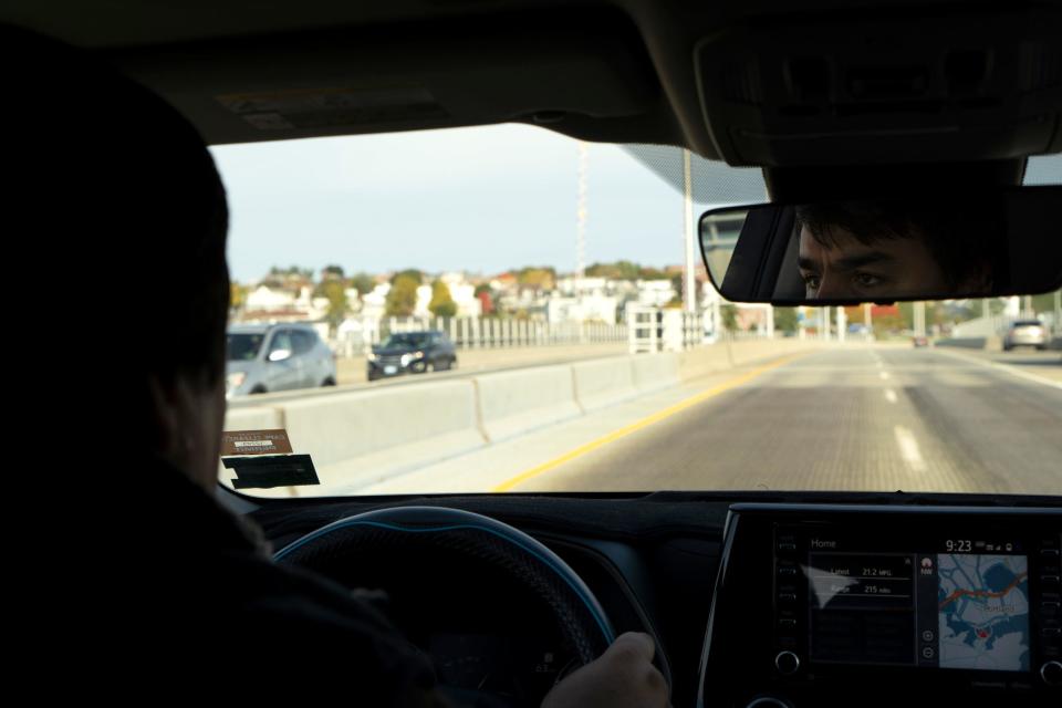 A road is seen ahead from the backseat of a car.
