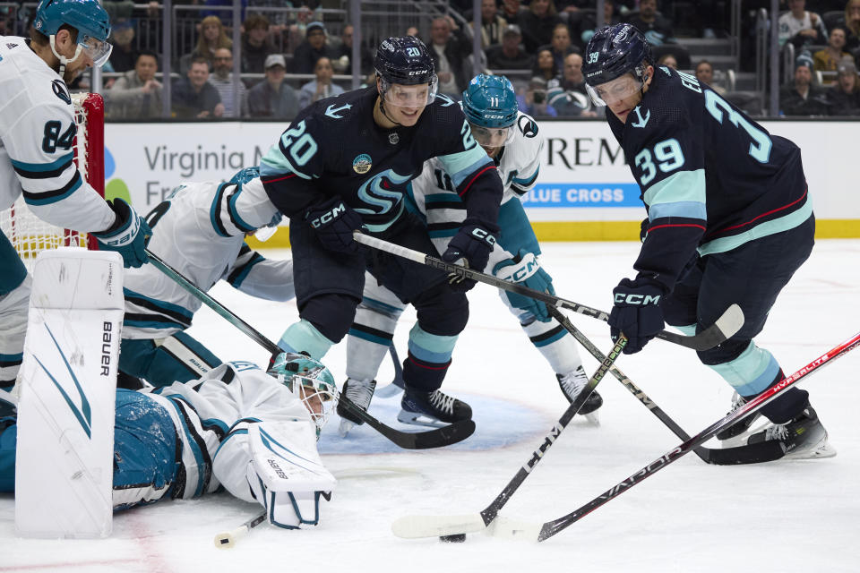 Seattle Kraken defenseman Ryker Evans (39) reaches for the puck on a shot blocked by San Jose Sharks goaltender Devin Cooley, bottom left, with Kraken right wing Eeli Tolvanen (20) assisting during the first period of an NHL hockey game, Thursday, April 11, 2024, in Seattle. (AP Photo/John Froschauer)