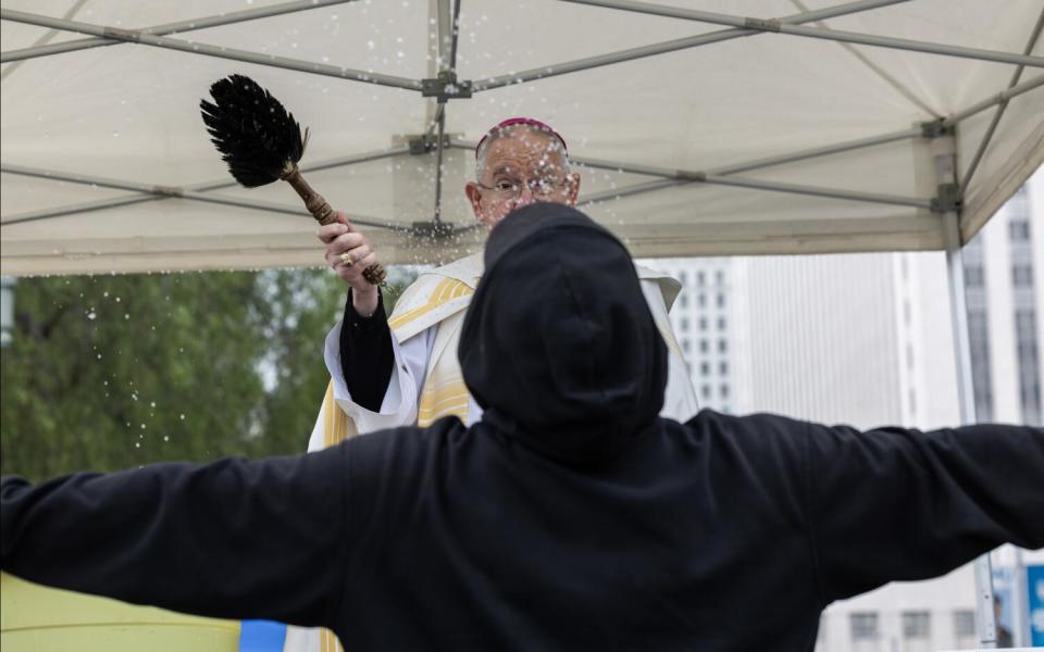 An archbishop splashes water on a man with outstretched arms