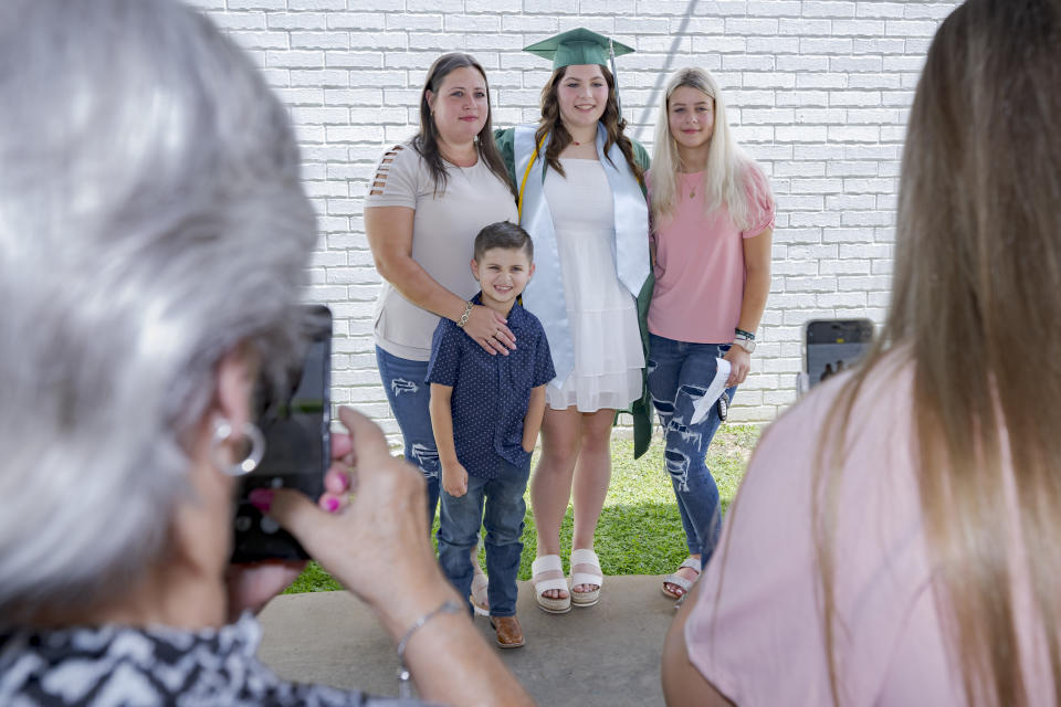 Khyli Barbee, 15, wearing mortar cap, poses for pictures with family and friends after graduating with the class of Springfield Preparatory School at Victory in Christ church in Holden, La., Saturday, Aug. 5, 2023. Nearly 9,000 private schools in Louisiana don’t need state approval to grant degrees. Non-approved schools make up a small percentage of the state total. But the students in Louisiana’s off-the-grid school system are a rapidly growing example of the national fallout from COVID-19 — families disengaging from traditional education. (AP Photo/Matthew Hinton)
