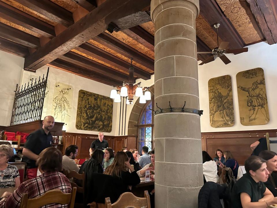 inside a restaurant with tables full under a midieval wood beam ceiling