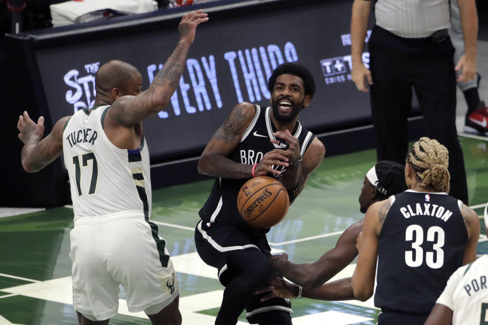 Brooklyn Nets' Kyrie Irving controls the ball as he drives between Milwaukee Bucks' P.J. Tucker (17) and Jrue Holiday during the first half of an NBA basketball game Tuesday, May 4, 2021, in Milwaukee. (AP Photo/Aaron Gash)