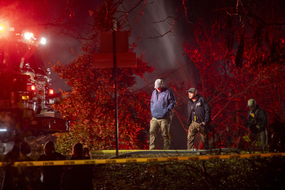 Fire and police officials walk around the scene of a house explosion as an Arlington County Fire Department ladder truck sprays water down on the remains of the building on Monday, Dec. 4, 2023, in Arlington, Va. (AP Photo/Kevin Wolf)