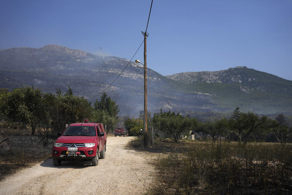 Vehicles with firefighters patrol as a helicopter drops water over a wildfire atop Mount Parnitha, in northwestern Athens, Greece, Thursday, Aug. 24, 2023. A major wildfire burning on the northwestern fringes of the Greek capital has torched homes and is now threatening the heart of a national park of Parnitha, one of the last green areas near the Greek capital. (AP Photo/Thanassis Stavrakis)