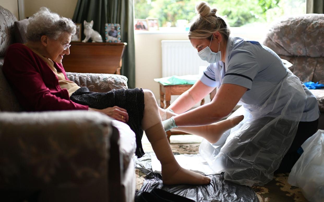 A nurse, wearing personal protective equipment changes the dressings on the legs of an elderly woman - PA