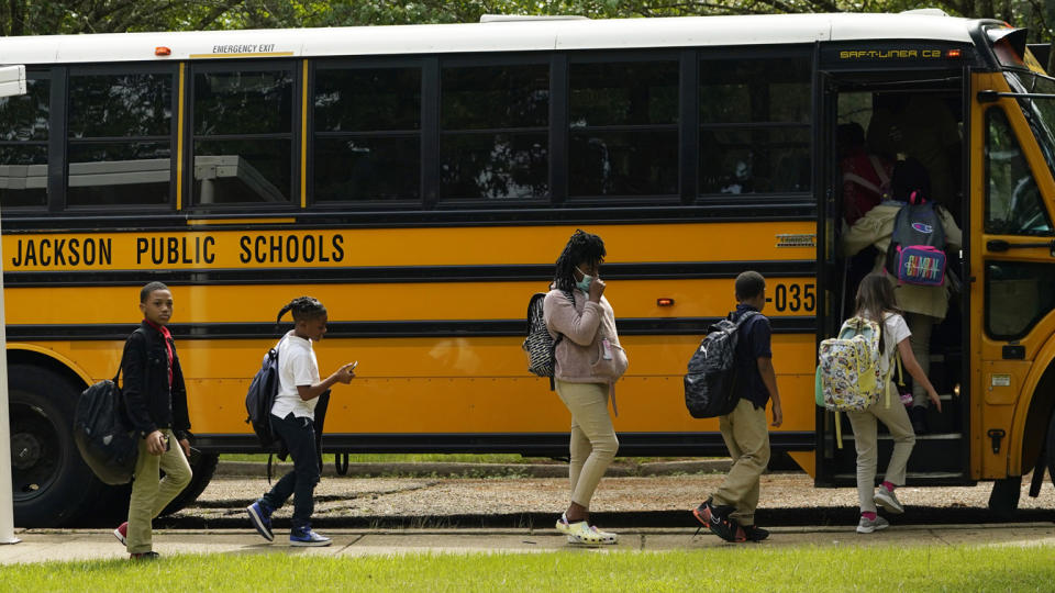 Children wearing backpacks board a school bus labeled Jackson Public Schools.