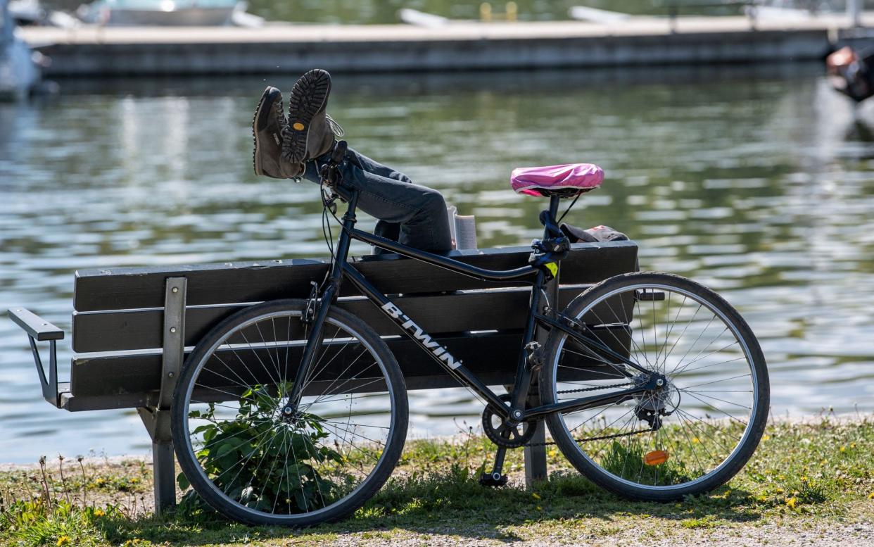 A man has parked his bicycle and takes a rest ejoying the sunny weather next to a canal at Djurgarden - Shutterstock