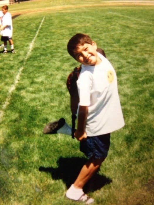 A boy in shorts, posing on the grass with one leg raised