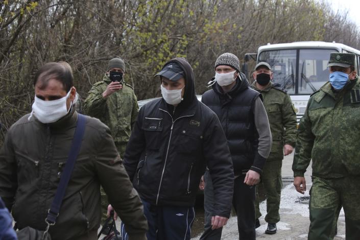 FILE - In this Thursday, April 16, 2020 file photo, Ukrainian war prisoners, wearing face masks to protect against coronavirus, escorted by Russia-backed separatist soldiers, also wearing face masks to protect against coronavirus, walk to be exchanged near the checkpoint Horlivka, eastern Ukraine. The United Nations human rights agency said in a report released Friday, July 2, 2021 that prisoners taken by the warring parties in the separatist conflict in eastern Ukraine have faced systematic torture, sexual violence and other abuses. (AP Photo/Alexei Alexandrov, File)