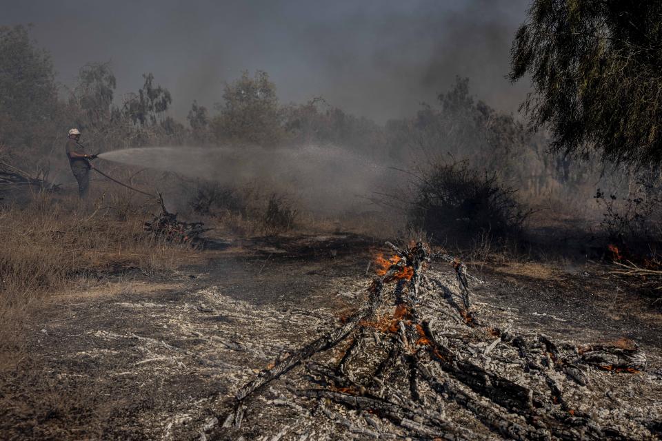 An Israeli firefighter attempts to extinguish a fire caused by a incendiary balloon launched by Palestinians from the Gaza Strip, on the Israeli side of the border between Israel and Gaza, Israel, Sunday, Aug. 16, 2020. (AP Photo/Tsafrir Abayov)