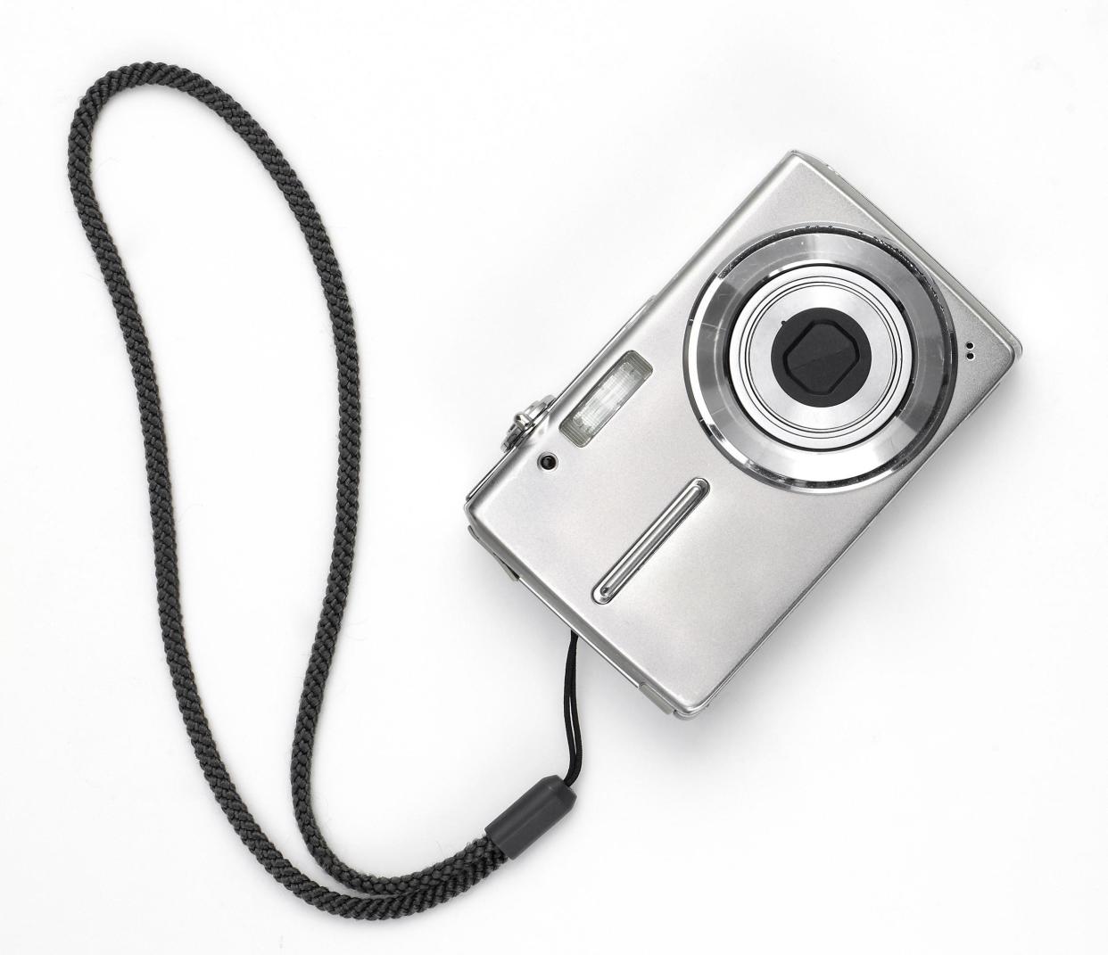 Simple chrome colored digital camera with black wristband, front facing with playful look against a white background