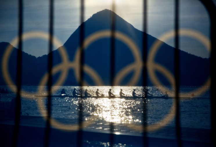 Rowers are seen through a screen decorated with the Olympic rings as they practice at the rowing venue in Lagoa at the 2016 Summer Olympics in Rio de Janeiro, Brazil, Aug. 7, 2016. (Photo: David Goldman/AP)