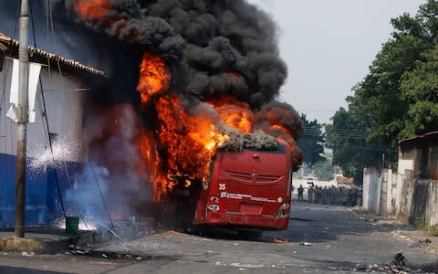 A bus that was torched during clashes with the Bolivarian National Guard burns in Urena, Venezuela - Credit: AP