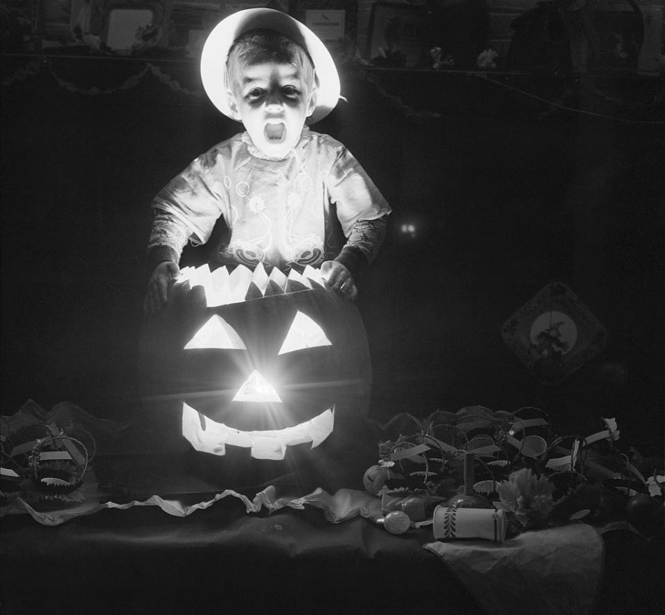 A child behind a lit-up Jack-o'-lantern