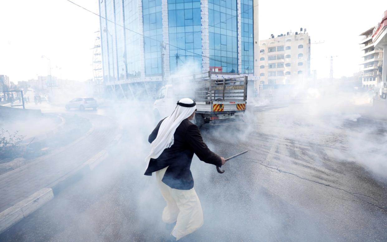 A Palestinian runs from tear gas fired by Israeli troops during a protest against the US embassy move near Ramallah - REUTERS