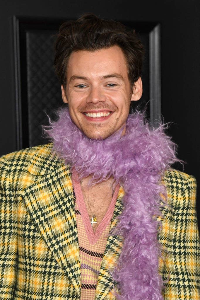 Harry smiling in a houndstooth jacket and feather boa at the Grammys