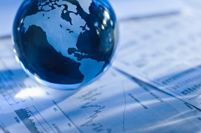 A small glass globe set atop paperwork displaying financial information and stock charts. 