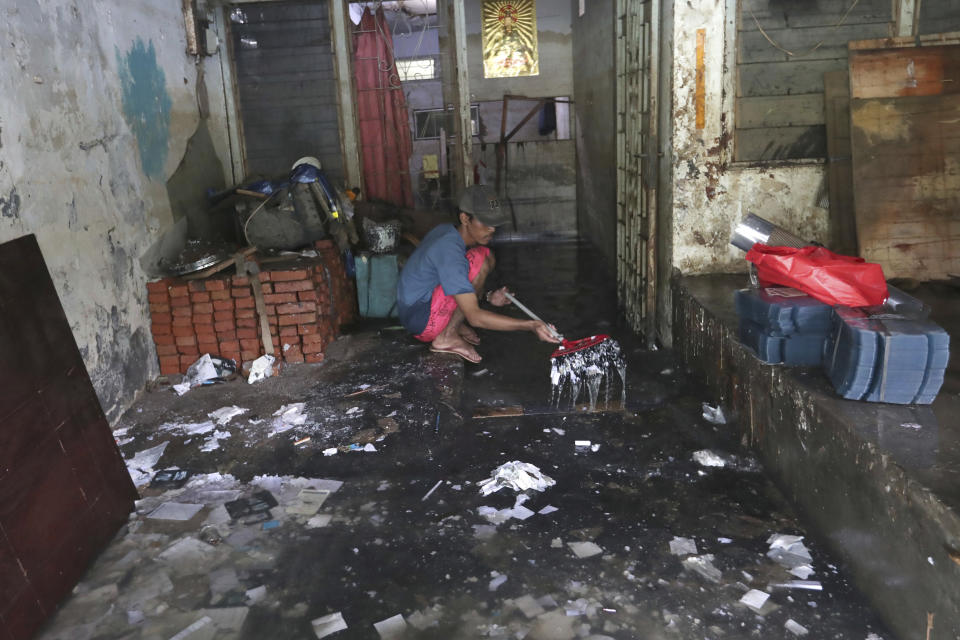 A man cleans his flood-damaged house in Jakarta, Indonesia, Sunday, Jan. 5, 2020. Landslides and floods triggered by torrential downpours have left dozens of people dead in and around Indonesia's capital, as rescuers struggled to search for people apparently buried under tons of mud, officials said Saturday. (AP Photo/Tatan Syuflana)