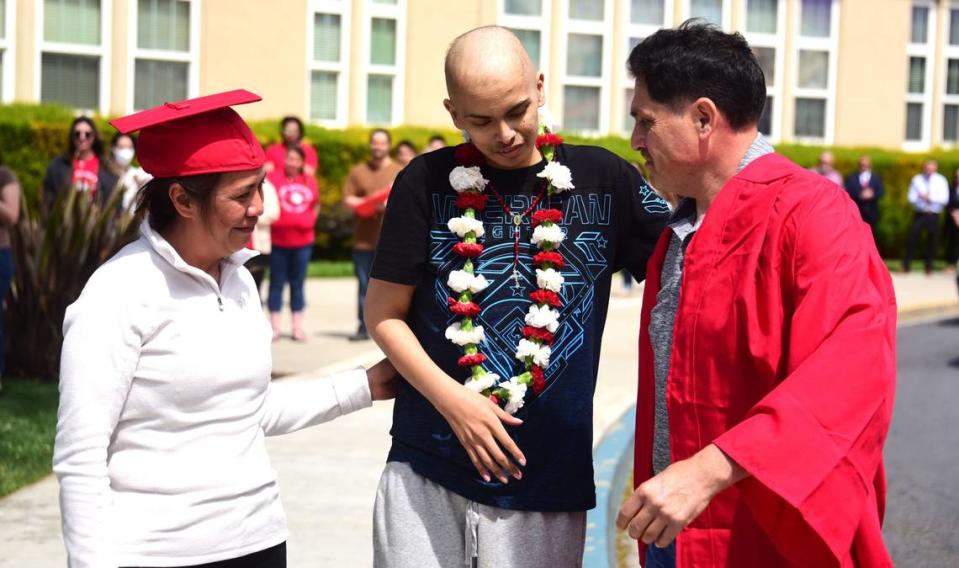 Brian Ortiz Núñez, alumno de último año de Gustine High School que está luchando contra un raro cáncer terminal, entrega su toga y su birrete de graduación a sus padres Luz María y Ramón, antes de posar para las fotos con ellos después de una ceremonia especial de graduación para Ortiz Núñez en Gustine High, en Gustine, California, el viernes 12 de abril de 2024.