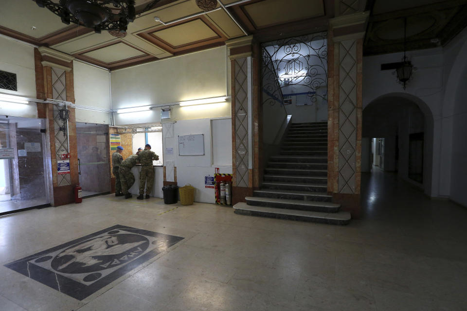 In this Friday, April 19, 2019, photo, U.N. peacekeepers stand at the reception desk at the Ledra Palace hotel inside the U.N. buffer zone in the divided capital Nicosia, Cyprus. This grand hotel still manages to hold onto a flicker of its old majesty despite the mortal shell craters and bullet holes scarring its sandstone facade. Amid war in the summer of 1974 that cleaved Cyprus along ethnic lines, United Nations peacekeepers took over the Ledra Palace Hotel and instantly turned it into an emblem of the east Mediterranean island nation's division. (AP Photo/Petros Karadjias)