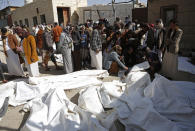 People look at the covered bodies of people that died in a Saudi-led coalition airstrike that killed at least 87 people, in a stronghold of Houthi rebels on the border with Saudi Arabia, in the northern Saada province of Yemen, Saturday, Jan. 22, 2022. Internet access remained largely down on Sunday after another Saudi-led coalition airstrike hit a telecommunications center Friday at the Red Sea port city of Hodeida. (AP Photo/Hani Mohammed)