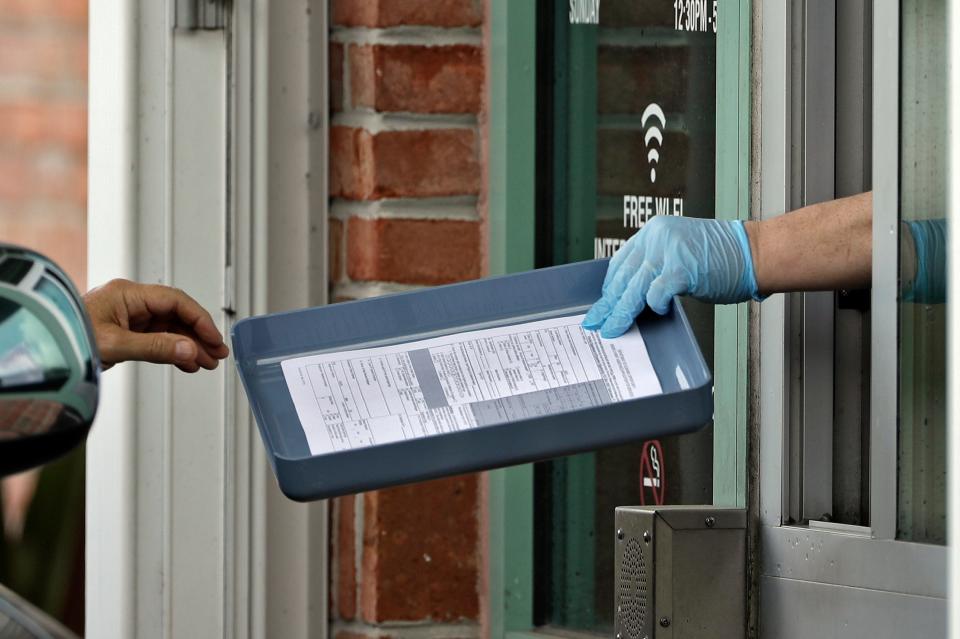 FILE - In this Friday, April 17, 2020 file photo, Hillsborough County Library Service employee Stephen Duran, right, wears gloves to protect himself from the coronavirus outbreak as he hands unemployment paperwork to residents at the Jimmie B. Keel Regional Library in Tampa, Fla. Federal data shows that Florida has processed its hundreds of thousands of new unemployment claims more slowly than any other state. (AP Photo/Chris O'Meara, File) ORG XMIT: FLWL203