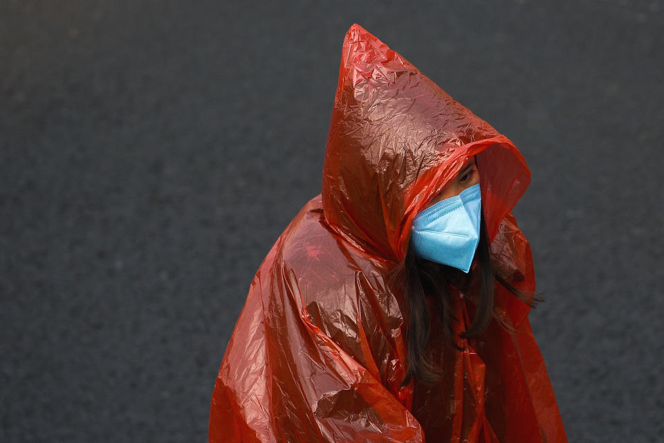 A masked woman in a plastic rain coat walks on a street in Beijing, Tuesday, Feb. 11, 2020. China's daily death toll from a new virus topped 100 for the first time and pushed the total past 1,000 dead, authorities said Tuesday after leader Xi Jinping visited a health center to rally public morale amid little sign the contagion is abating. (AP Photo/Andy Wong)