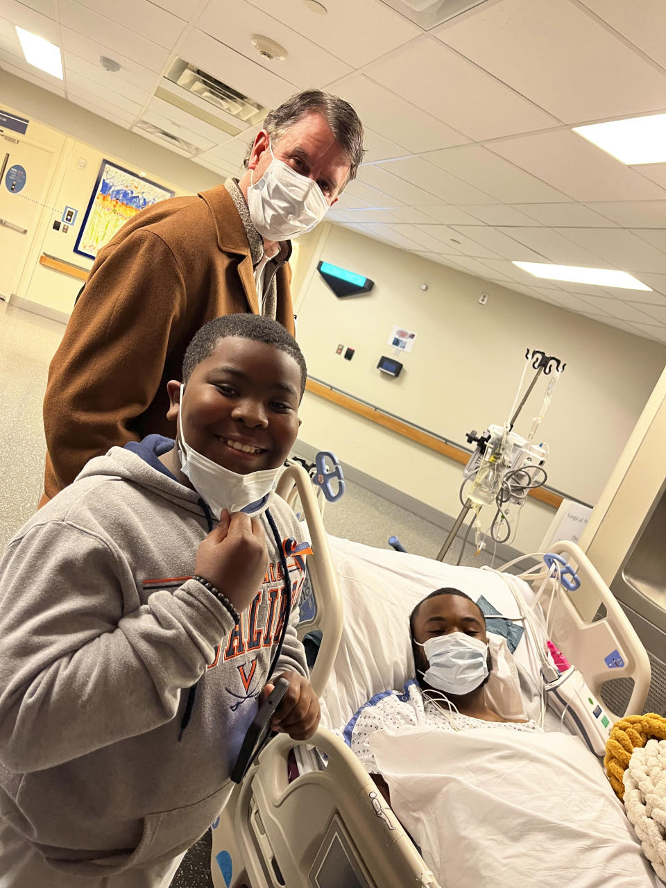 This image provided by Brenda Hollins by Gordon McKernan shows Mike Hollins, right, his younger brother, Deuce, and family friend McKernan pose for a photo at the University of Virginia Medical Center in Charlottesville, Va., on Wednesday, Nov. 17, 2022. Hollins was shot and wounded on the school’s campus on Sunday, Nov. 13. Three of his teammates on the university’s football team were fatally shot during the incident. (Brenda Hollins and Gordon McKernan via AP)