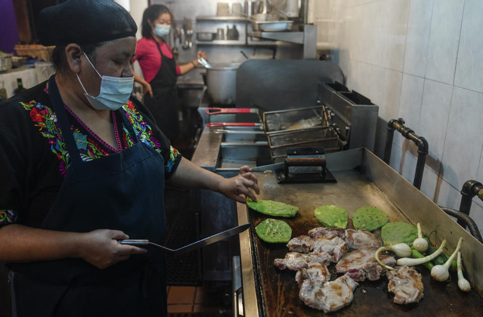 Natalia Méndez cooks a meal with pork chops, Jalapenos and cactus plants in the kitchen of La Morada, an award winning Mexican restaurant she co-owns with her family in South Bronx, Wednesday Oct. 28, 2020, in New York. After recovering from COVID-19 symptoms, the family raised funds to reopen the restaurant, which they also turned into a soup kitchen serving 650 meals daily. (AP Photo/Bebeto Matthews)