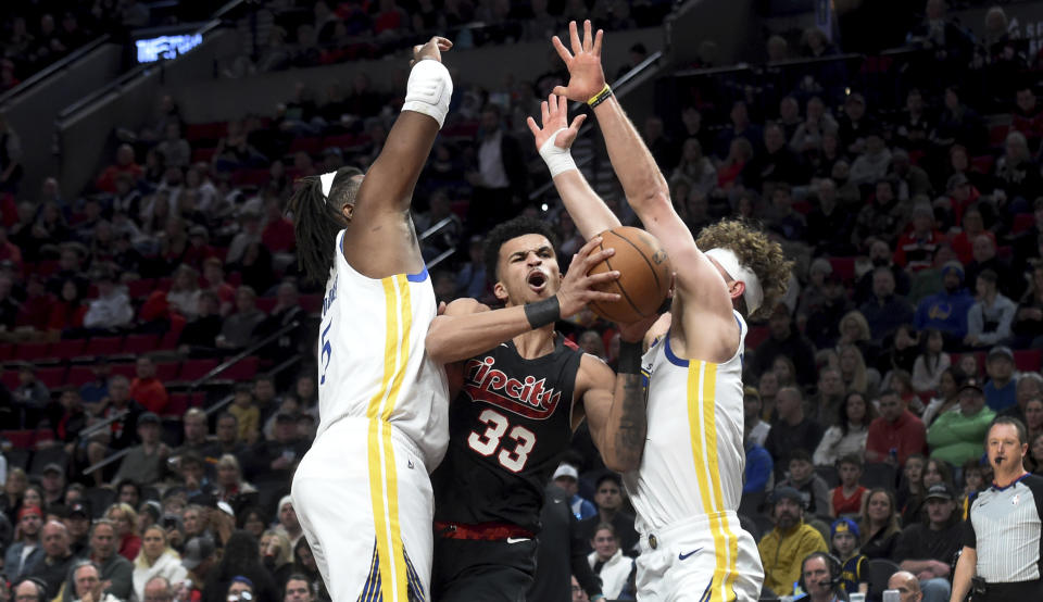 Portland Trail Blazers forward Toumani Camara (33) drives to the basket between Golden State Warriors forward Kevon Looney, left, and guard Brandin Podziemski, right, during the first half of an NBA basketball game in Portland, Ore., Sunday, Dec. 17, 2023. (AP Photo/Steve Dykes)