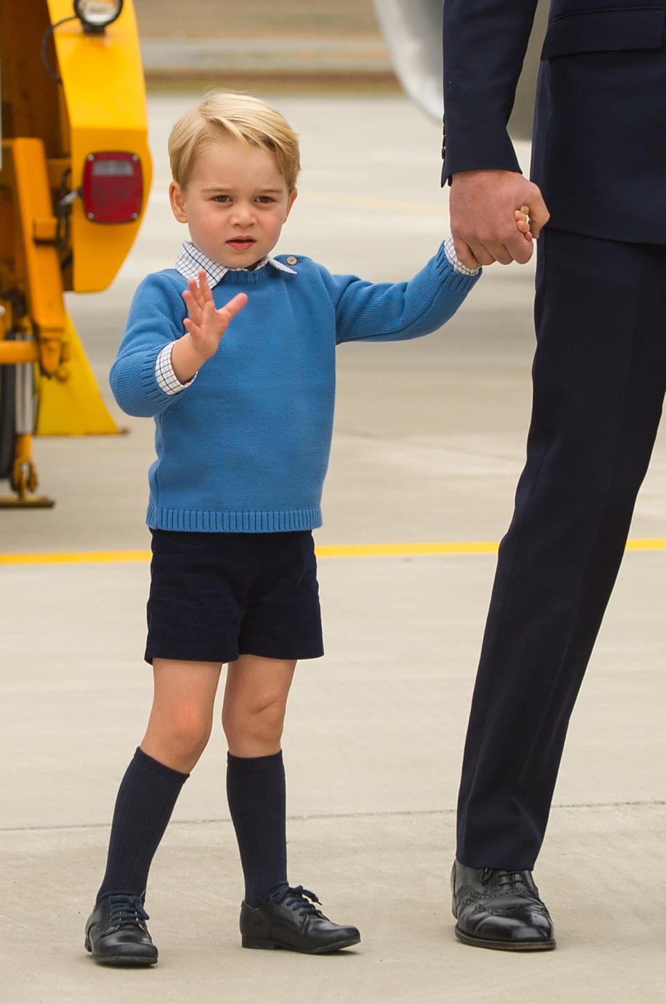 Prince George waving to the crowd wearing a blue sweater and knee-high socks. 