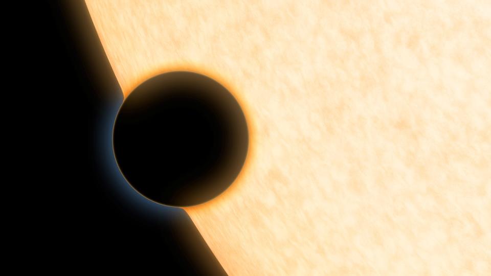 a large black circle passes in front of a close up view of a yellow star, there is a hazy orange glow around the black circle.