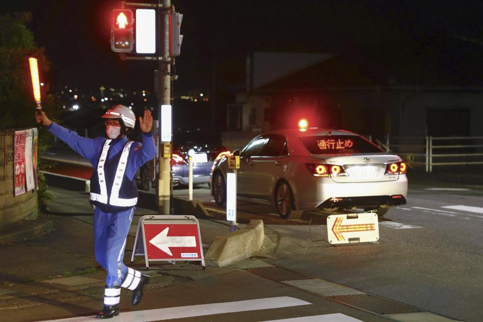 A police officer directs traffic near a building where a man is holed up in Nakano, central Japan, Thursday, May 25, 2023. Multiple people including a few police officers were killed in Nakano, a city in Nagano prefecture, in central Japan on Thursday and a suspect with a rifle and knife was holed up inside a house, police said. (Takuto Kaneko/Kyodo News via AP)