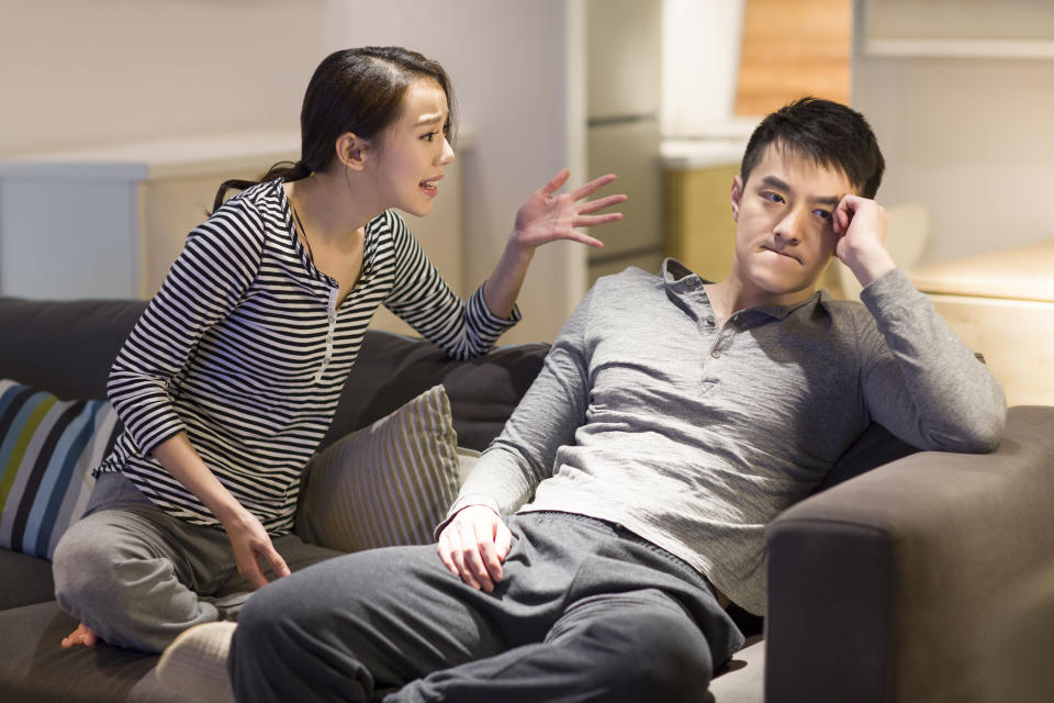 A woman in striped casual wear sits on a couch, gesturing and speaking to a man who is reclining, looking away with his hand on his face