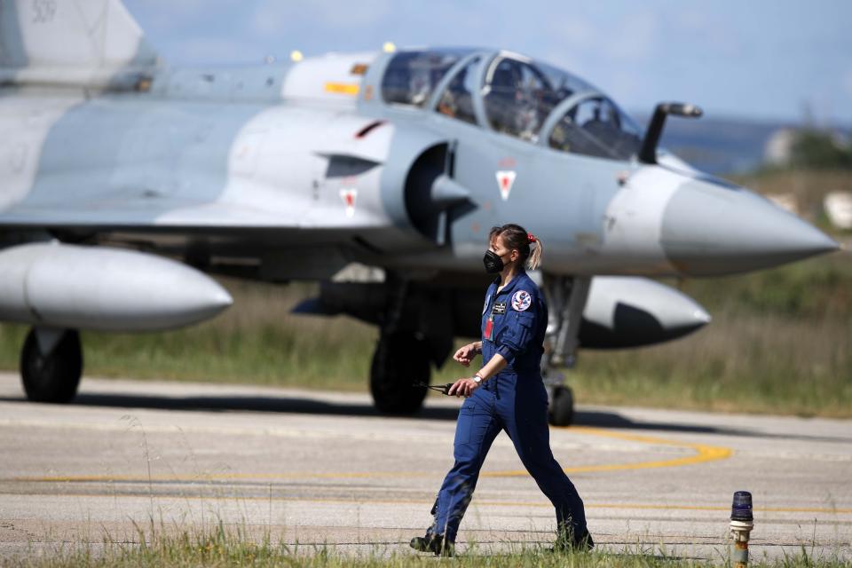 An air force officer walks as a Greek fighter jet Mirage 2000-5 taxis during the international military exercise Iniochos at Andravida air base, about 279 kilometres (174 miles) southwest of Athens, Tuesday, April 20, 2021. Greece vowed Tuesday to expand military cooperation with traditional NATO allies as well as Middle Eastern powers in a race to modernize its armed forces and face its militarily assertive neighbor Turkey. (AP Photo/Thanassis Stavrakis)