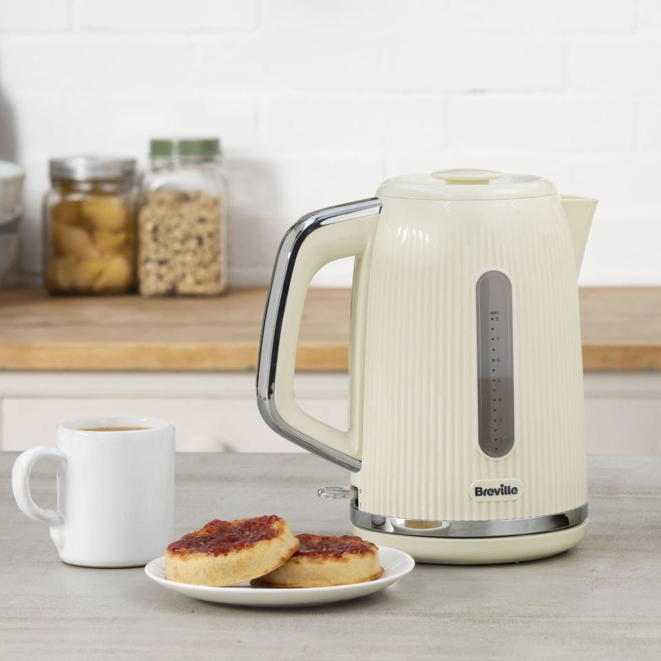 Cream Breville kettle next to cup of tea and crumpets with jam