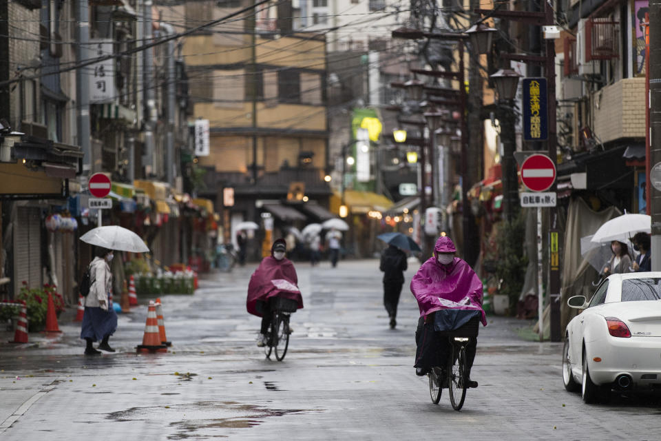 People walk and ride bicycles through a street lined with temporarily closed restaurants and bars due to the coronavirus state of emergency measures in Tokyo on Thursday, April 29, 2021. (AP Photo/Hiro Komae)