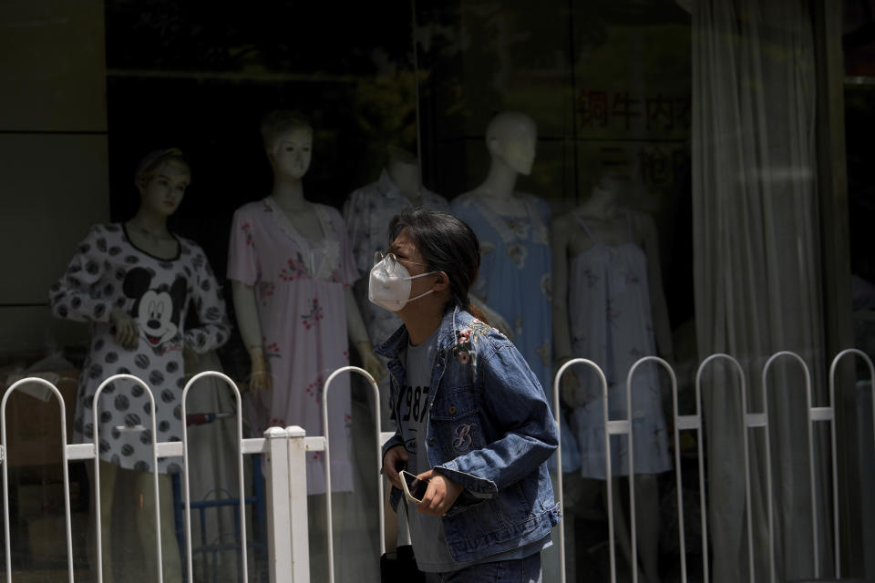 A woman wearing a face mask walks by a barricaded retail shop selling pajamas that has been locked down as part of COVID-19 controls in Beijing, Tuesday, June 14, 2022. Authorities ordered another round of three days of mass testing for residents in the Chaoyang district following the detection of hundreds coronavirus cases linked to a nightclub. (AP Photo/Andy Wong)