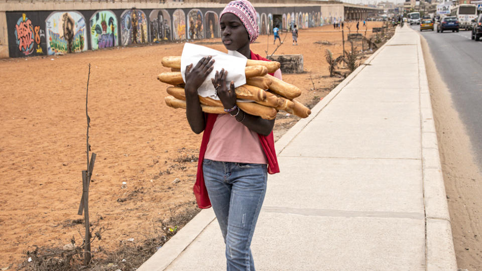 A woman carries baguettes bread along a road in Dakar, Senegal - February 2024