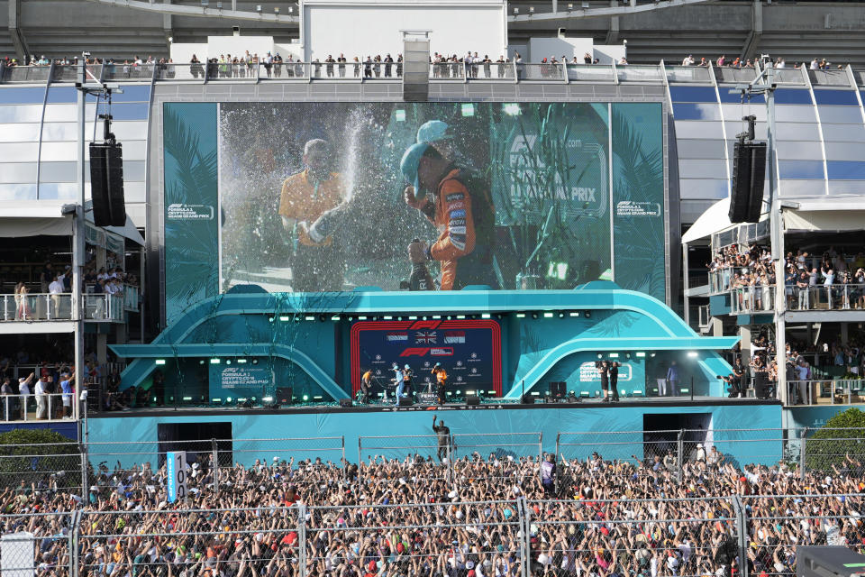 McLaren driver Lando Norris, of Britain, on monitor, is sprayed with champagne as he stands on the podium after winning the Formula One Miami Grand Prix auto race at the Miami International Autodrome, Sunday, May 5, 2024, in Miami Gardens, Fla. (AP Photo/Wilfredo Lee)