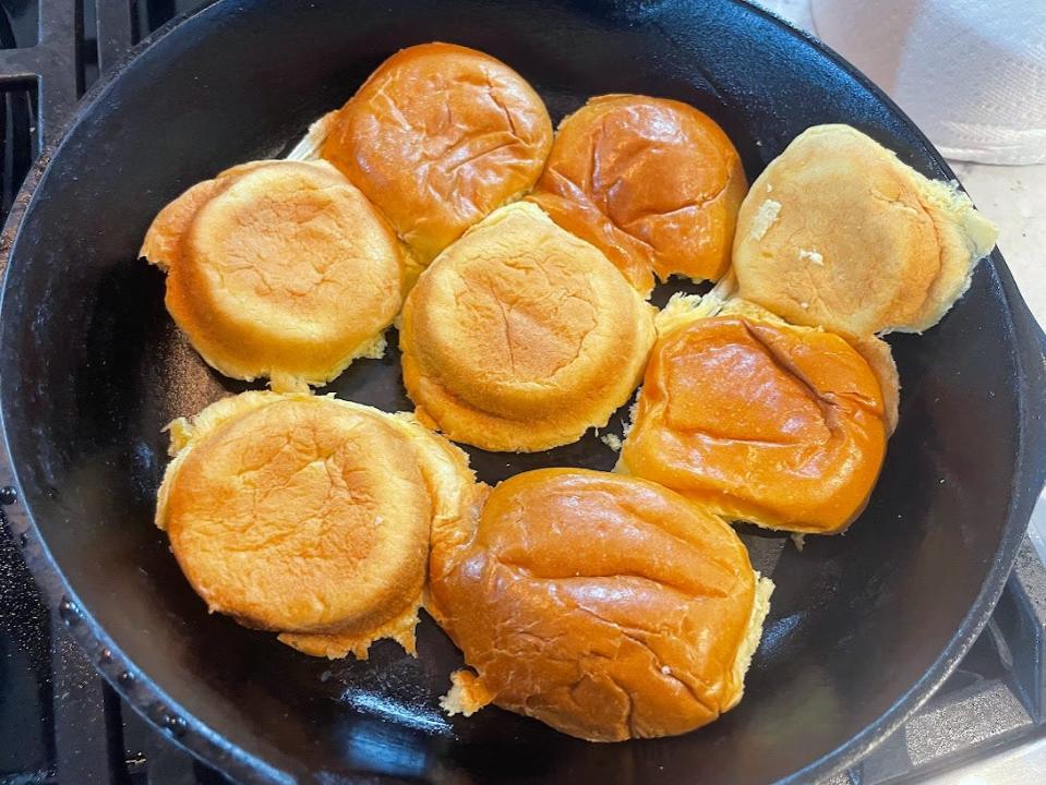 Several small brioche buns place cut-side down on a skillet