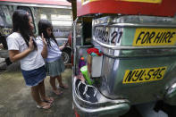 Grade school students Bhea Joy Roxas, right, and Elrich Joy, left, use a smart phone as they raise their hands while reciting the "Panatang Makabayan" or Patriotic Oath during the opening of classes at the Tandang Sora jeepney terminal in Quezon city, Philippines on Monday, Oct. 5, 2020. Students in the Philippines began classes at home Monday after the coronavirus pandemic forced remote-learning onto an educational system already struggling to fun schools. The two students missed the flag raising ceremony due to poor internet connection. (AP Photo/Aaron Favila)