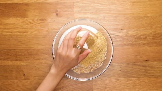 Adding seasame seeds to chopped peanuts and sugar in a glass bowl