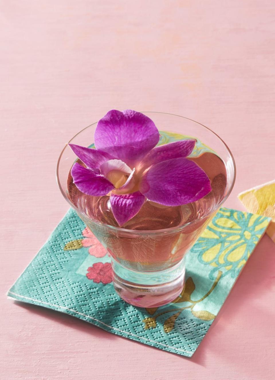 martini in stemless glass with purple orchid flower on top and blue floral napkin